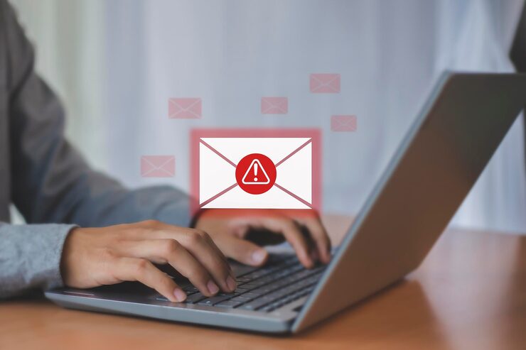 A person typing on a laptop with a warning email icon in red above them. 